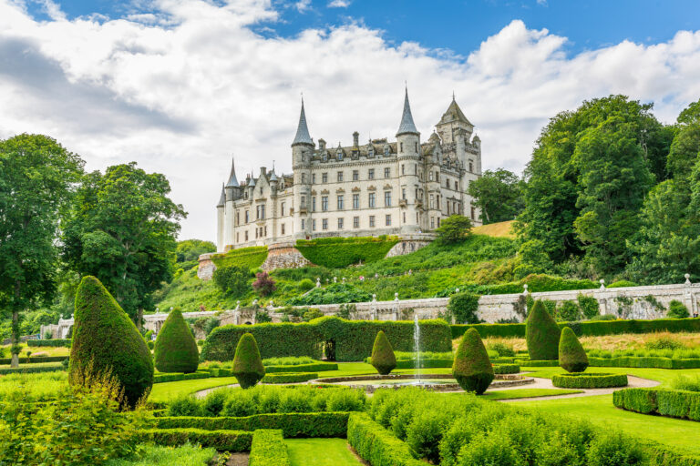 A view of Dunrobin Castle, with lush greenery in the foreground and a water fountain spraying water into the sky